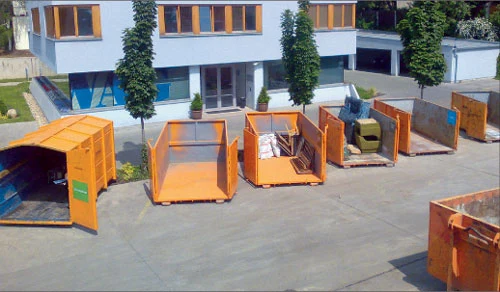 Řada oranžových kontejnerů na recyklaci plných odpadu před budovou.