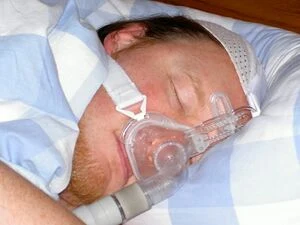 Muž spí s přístrojem na dýchání pro léčbu obstrukční spánkové apnoe.