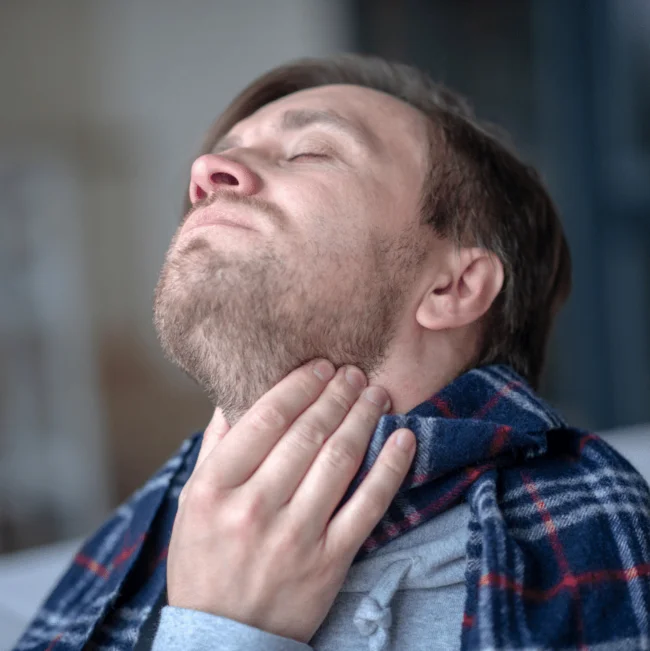 Muž s bolestmi v krku drží ruku na hrdle.