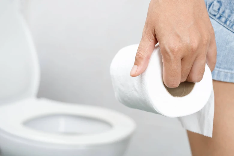 Ruka drží toaletní papír před otevřeným záchodem.