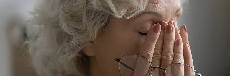 Starší žena zakrývá oči rukama v bolesti.