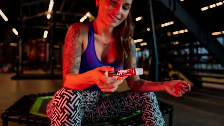 Žena v posilovně drží tubu s hořčíkem pro prevenci křečů