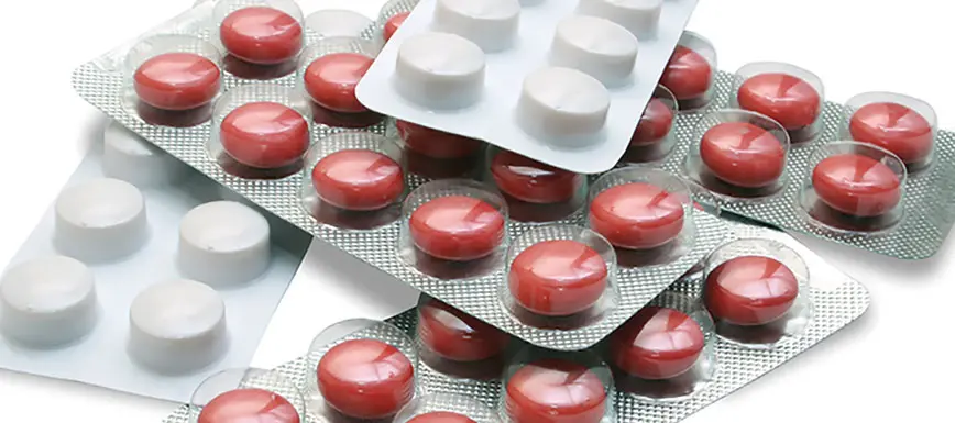 Červené a bílé tablety antibiotik v bublinkovém obalu.
