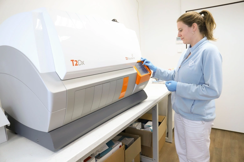 Žena v modrém oblečení ovládá lékařský analyzátor pro diagnostiku.