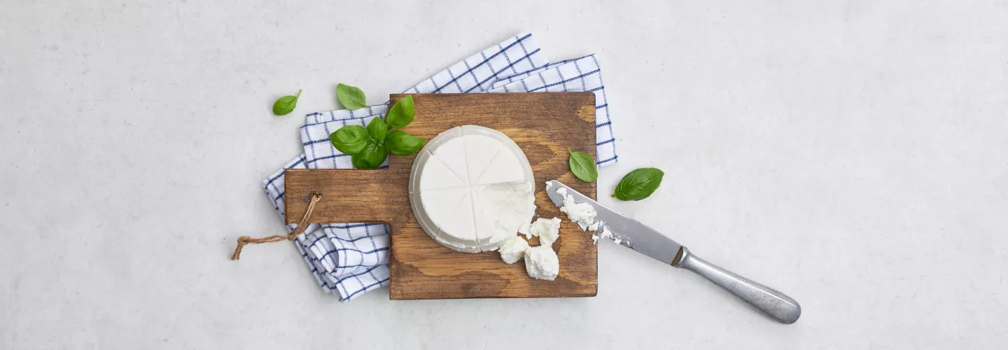 Kolo sýra Ricotta na dřevěném prkénku se bazalkou.