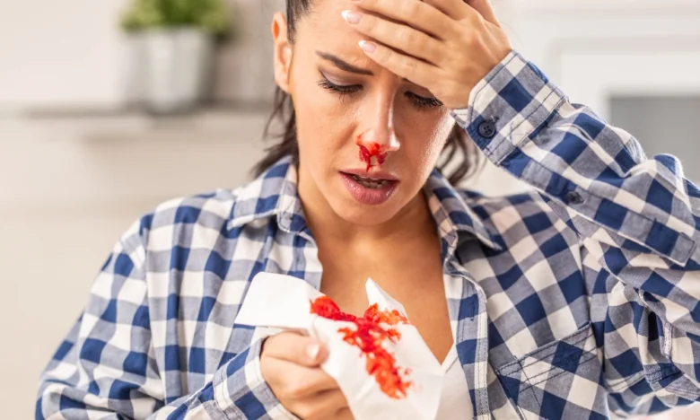 Žena s krvácením z nosu drží kapesník u obličeje.