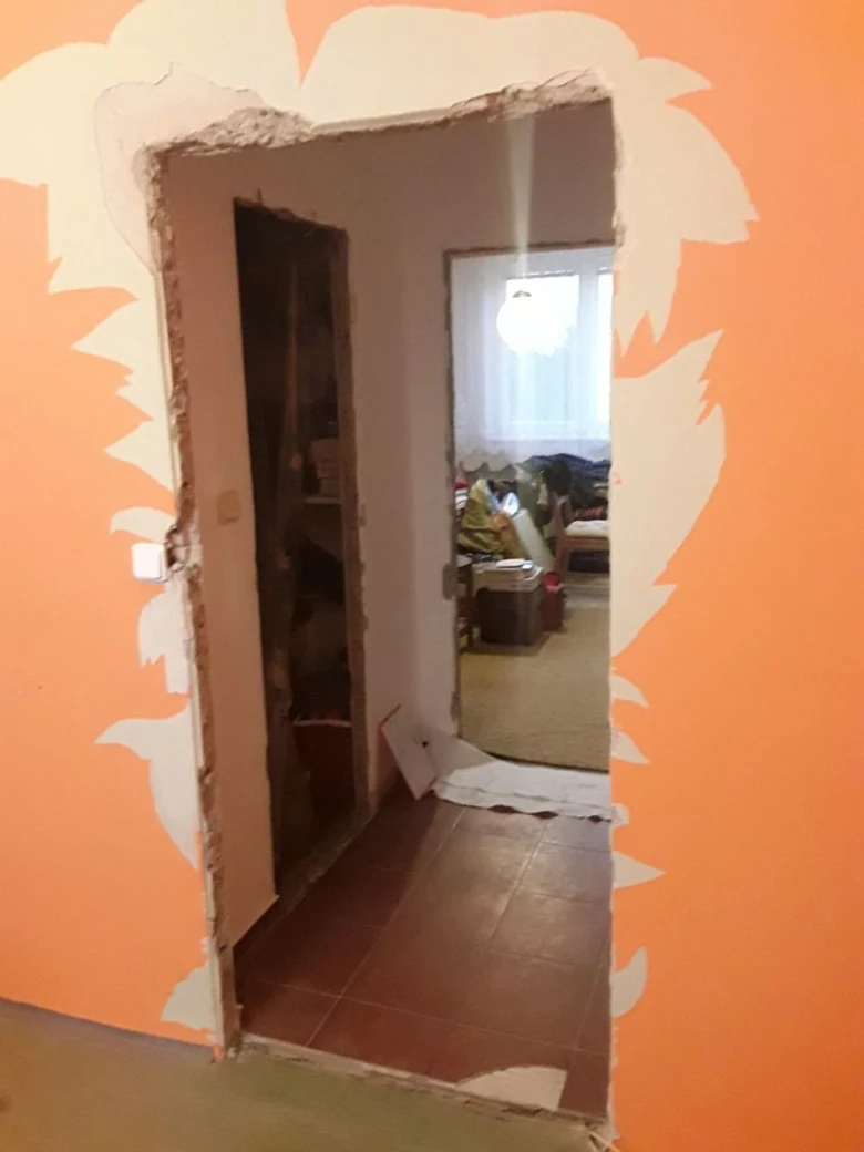 Vybouraná zárubeň s odhaleným rámem v oranžové stěně.