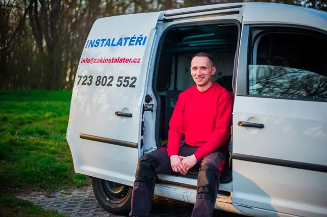 Instalatér sedí v otevřené dveři svého bílého služebního vozu.