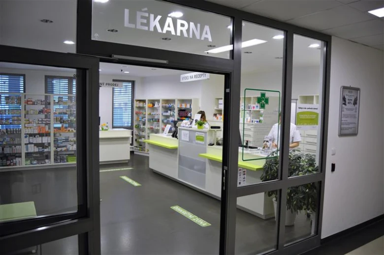 Vstup do lékárny s viditelnými regály a pracovníkem u pultu.