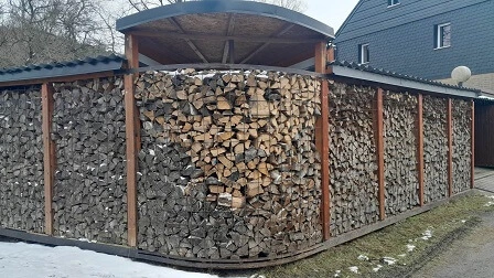 Dřevník svépomocí s uspořeným dřívím pod střechou.
