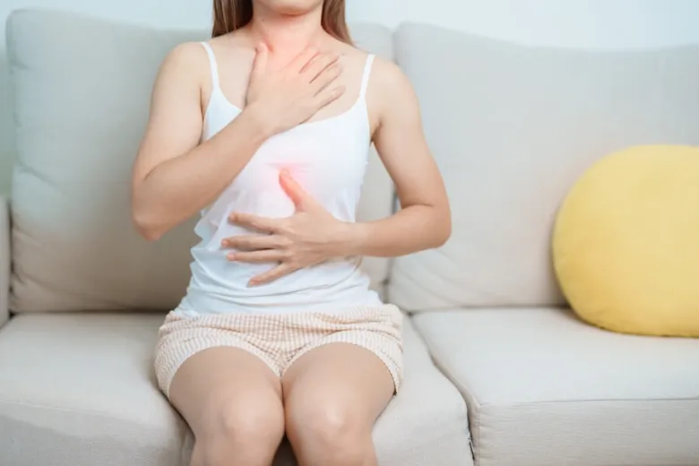 Žena sedí na gauči a drží si hrudník kvůli pálení žáhy.
