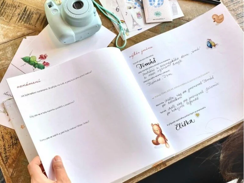 Roztehlá knížka s českými jmény pro dítě vedle fotoaparátu.