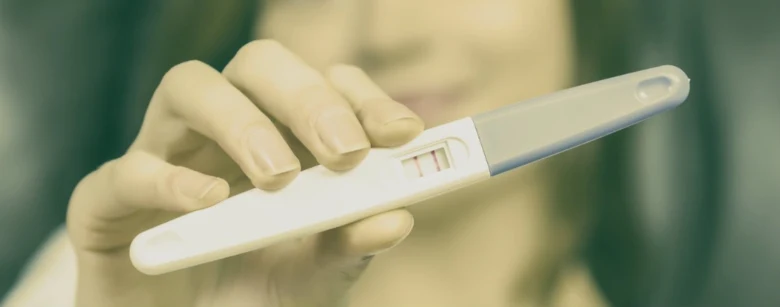 Ruka drží těhotenský test s viditelným pozitivním výsledkem.