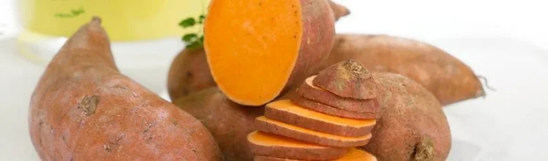 Celé batáty s řezem ukazující oranžovou dužinu na bílém podkladu.