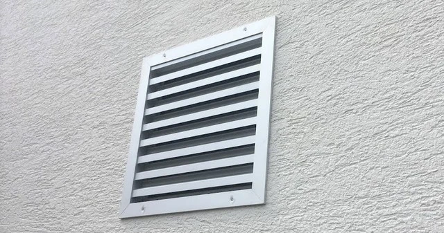 Bílá větrací mřížka s horizontálními lamelami na zdivu.