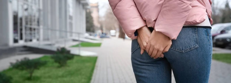 Osoba v džínách stojí na chodníku s rukama mezi nohama.