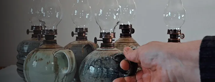 Ruka drží keramickou petrolejovou lampu mezi dalšími lampiony.