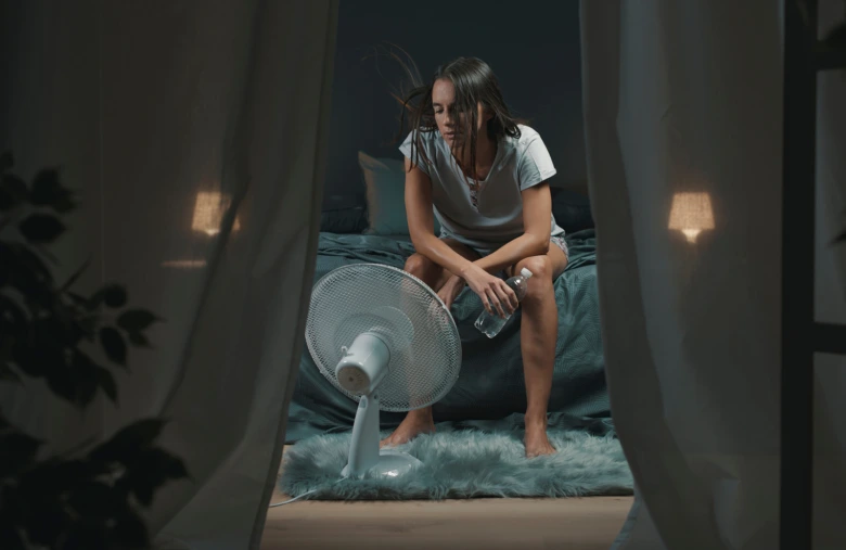 Žena sedí v posteli s potem na čele při nočním pocení.