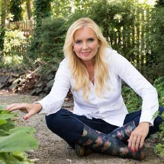 Žena sedí v zahradě mezi rostlinami a ukazuje na ně.