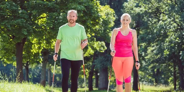 Muž a žena chodí venku s hůlkami pro nordic walking.