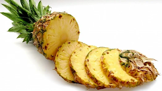 Kusovaný zralý ananas s korunou na bílém pozadí.