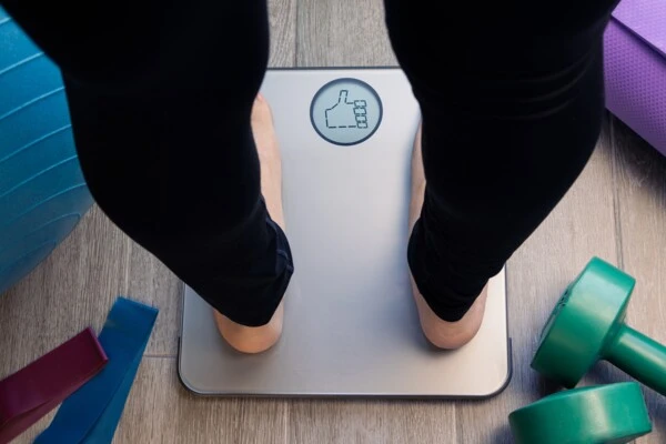Osoba stojí na váze v domácnosti s fitness vybavením.