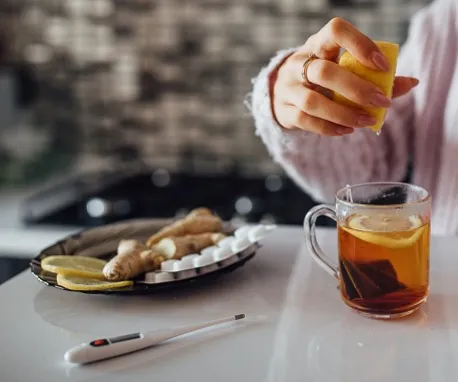 Člověk stlačí citron do čaje s ingverem pro domácí léčbu.