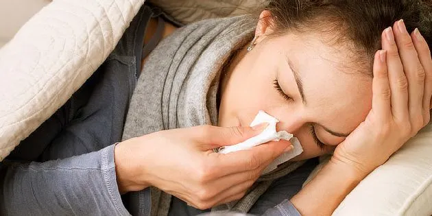 Žena leží v posteli s chřipkou a dýchá do kapesníku.