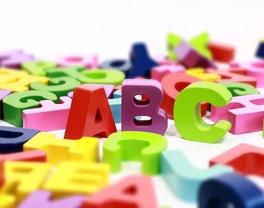 Kolorované dřevěné písmena ABC rozsypané na bílém pozadí.