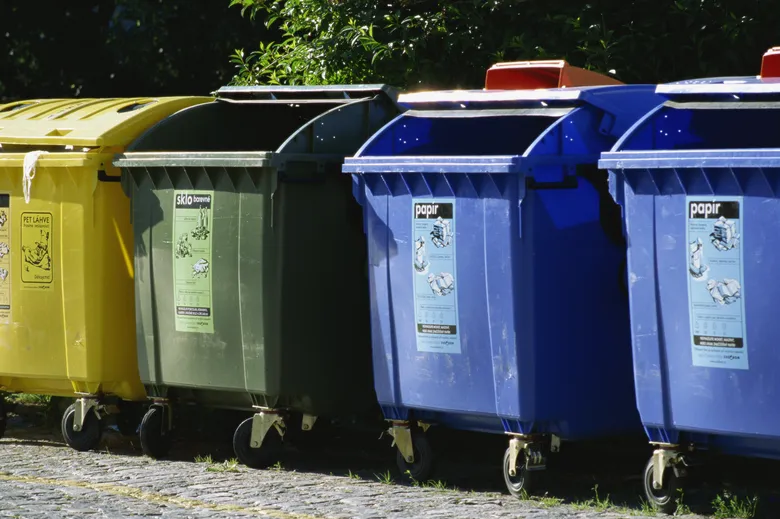 Řada barevných kontejnerů na třídění odpadu venku.