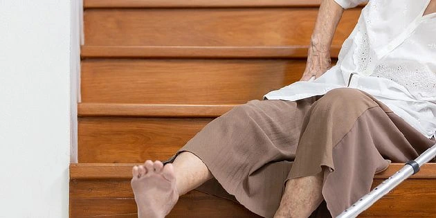 Starší osoba sedí na schodech s křeslem kvůli osteoporóze.