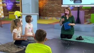 Žena ukazuje znakovou řeč dětem v učebně.