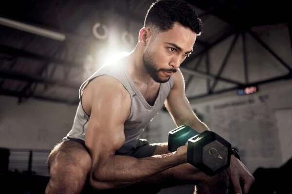 Muž v posilovně zvedá činku pro trénice biceps.