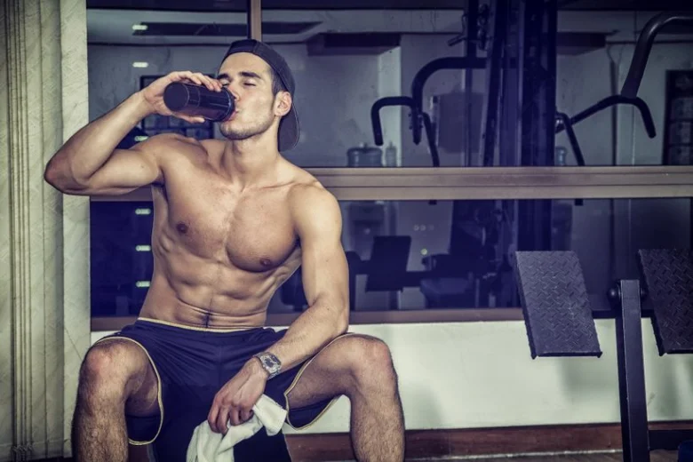 Muž v posilovně pije proteinový nápoj po tréninku.