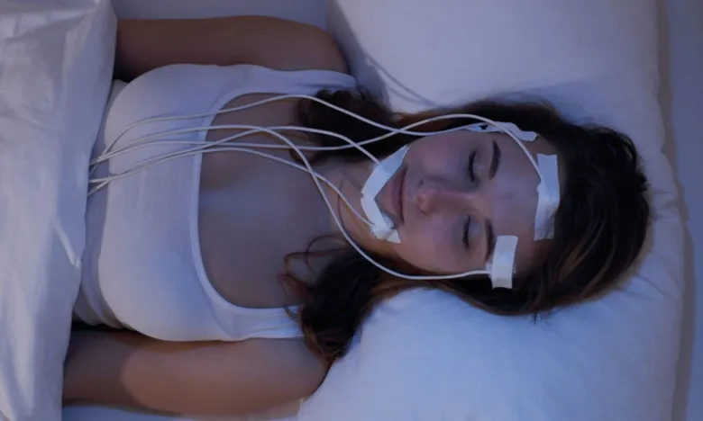 Žena spí s elektrodami na obličeji pro monitorování fází spánku.