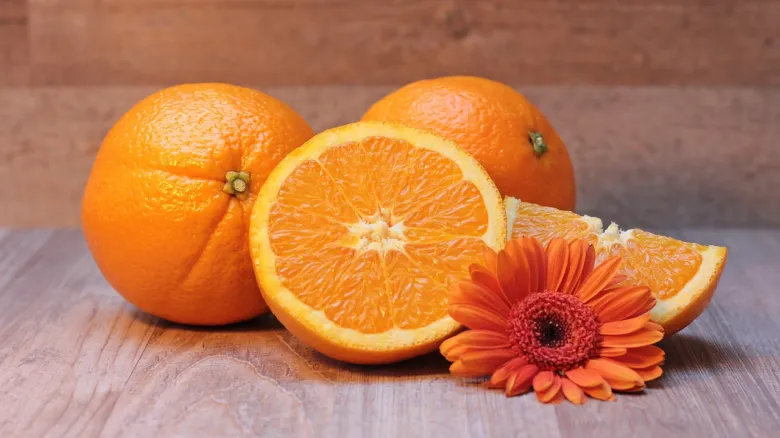 Celé pomeranče s řezem a oranžová květina na dřevě.