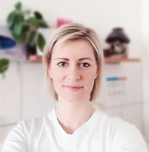 Portrét ženy v bílé košili s krátkými blond vlasy.