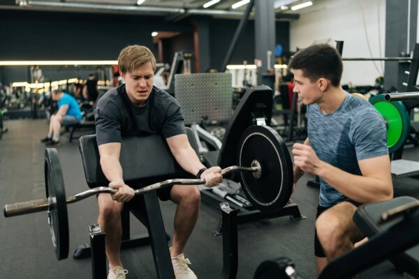 Muž dělá bicepsového zvedání s trénerem v posilovně.