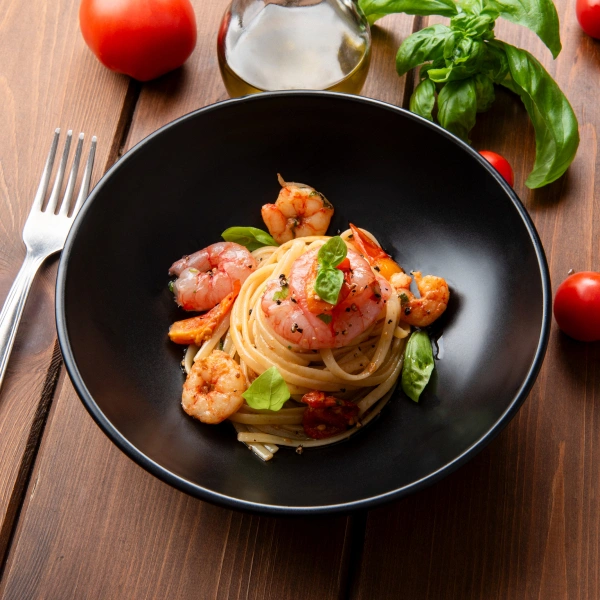 Pasta s krevetkami a čerstvou bazalkou v černé misce.