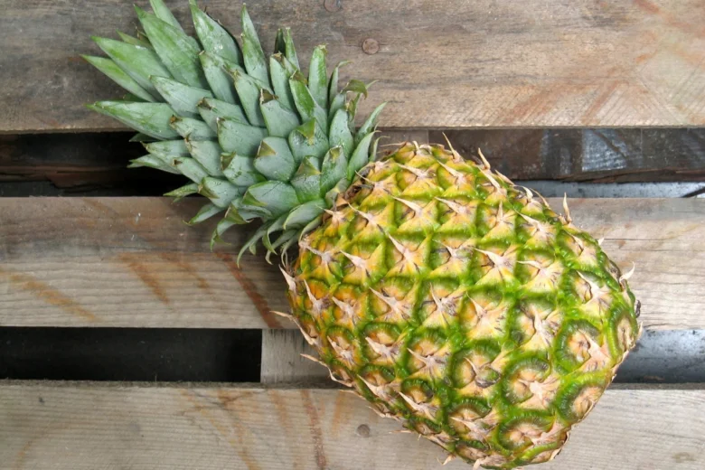 Celý ananas s zelenou korunou na dřevěném povrchu.