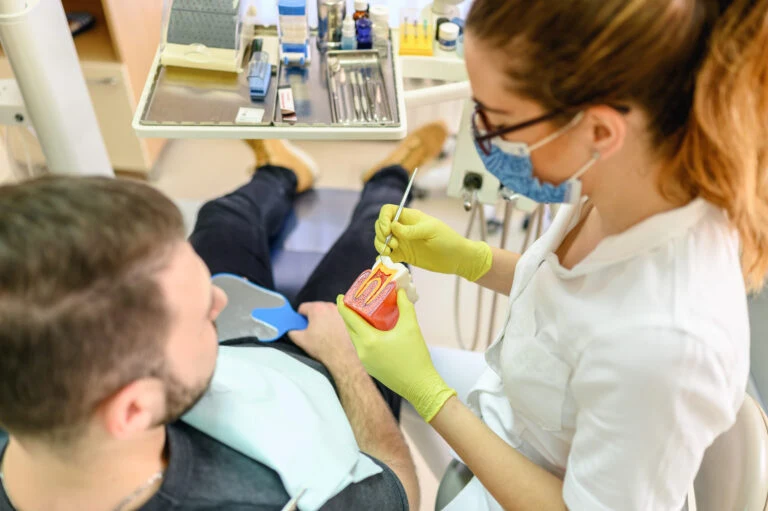 Zubní lékař ukazuje léčbu zánětu dásní na modelu úst.