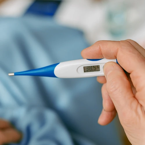 Digitální teploměr v ruce ukazující horečku při chřipce