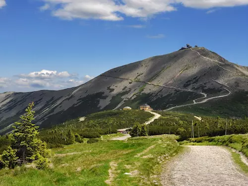 Zelená horská cesta vedoucí k vrcholu pod modrou oblohou.