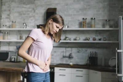 Žena v kuchyni drží břicho kvůli bolestivým křečím.