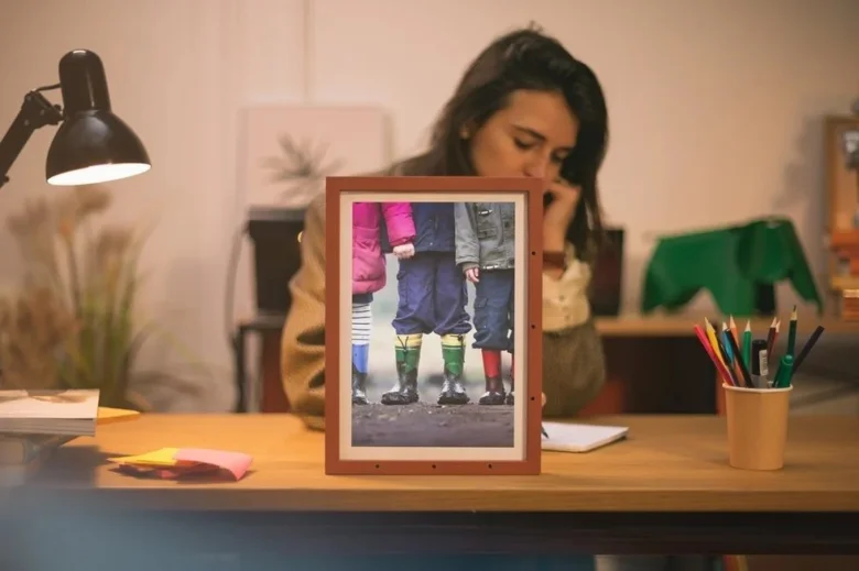 Žena pracuje u stolu s rámečkem dětí na stole.