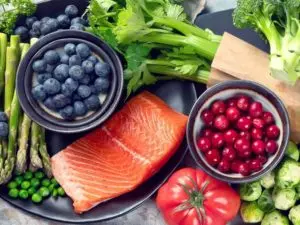Salmon svařené s bobulemi a zeleninou na tmavém talíři.