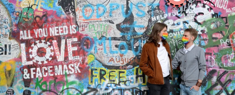 Dva lidé s deštníkovými rouškami před grafitovou zdí.