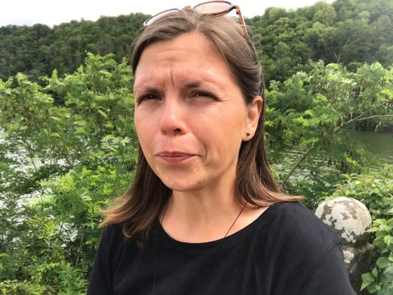 Žena stojí venku před zeleným lesem.