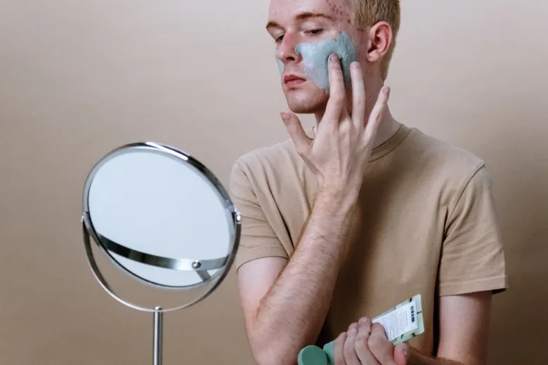 Muž nanáší modrou pleťovou masku na obličej s akné.