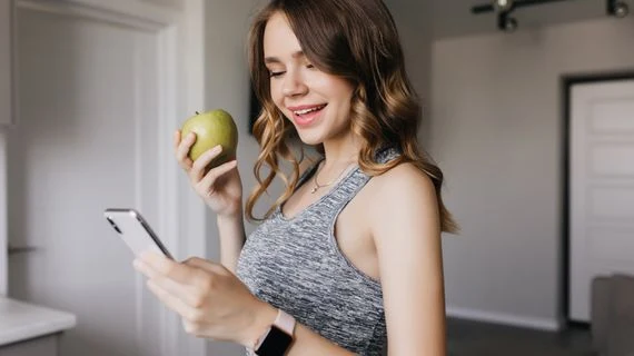 Žena drží jablko a kouká na telefon v interiéru.